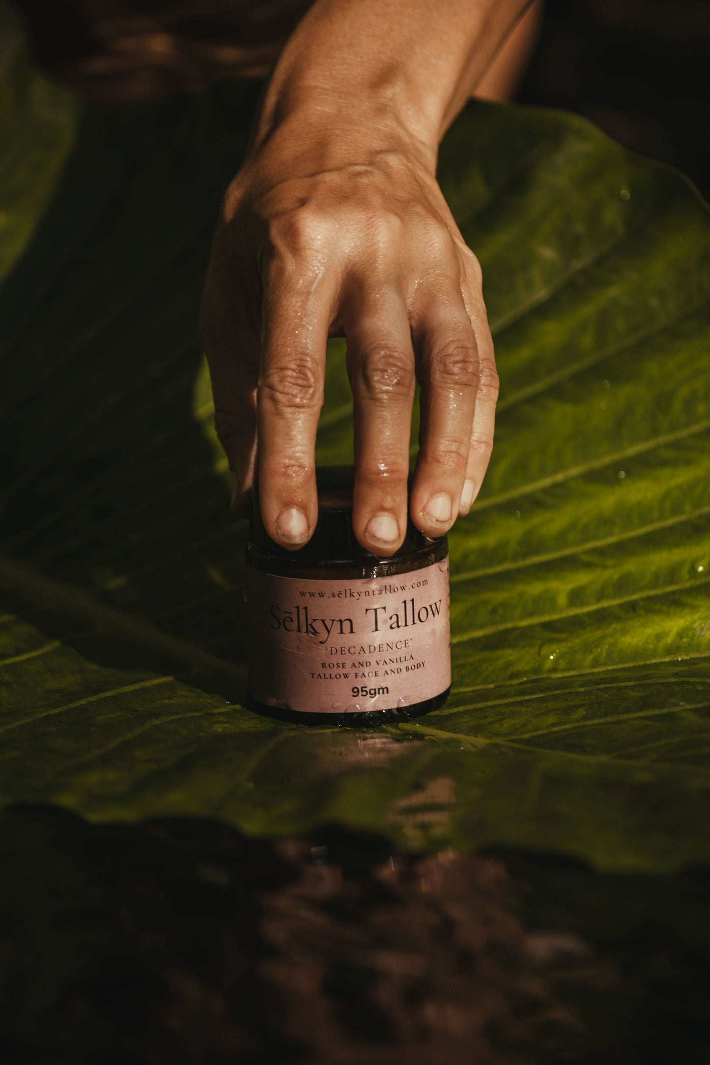 Hand placing Sēlkyn Tallow balm on natural surface with soft earthy lighting