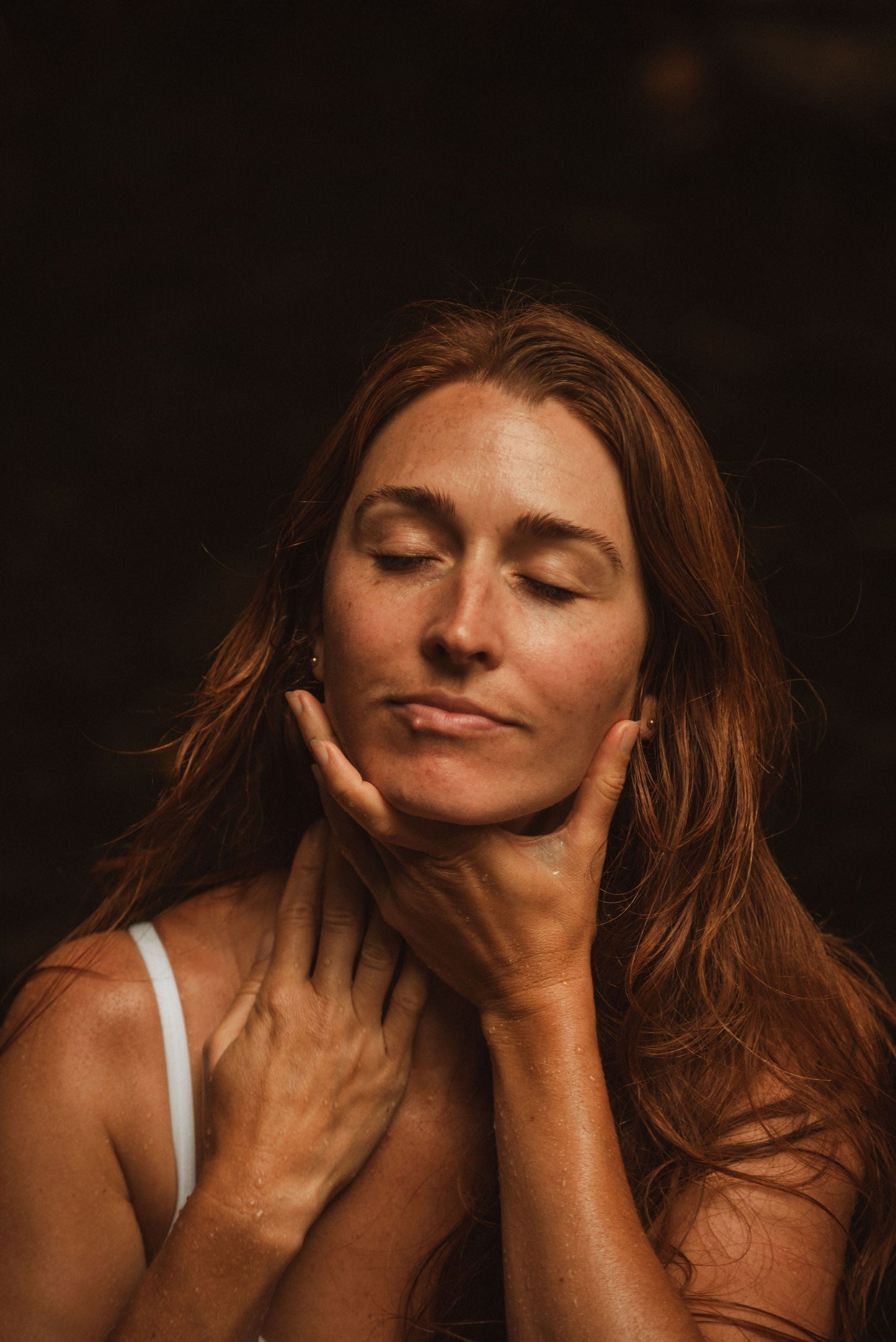 woman with glowing natural skin gently touching her face in soft light